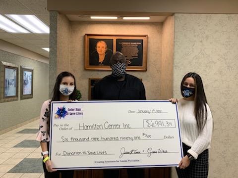 Giana White (left) and Jillian Turner (right), co-managers of the Color Run to Save Lives, present a check to Melvin L Burks (center), CEO of Hamilton Center, in support of suicide prevention and mental health services. The event took place in early November and gathered 150 participants and 20 volunteers, raising nearly seven thousand dollars.